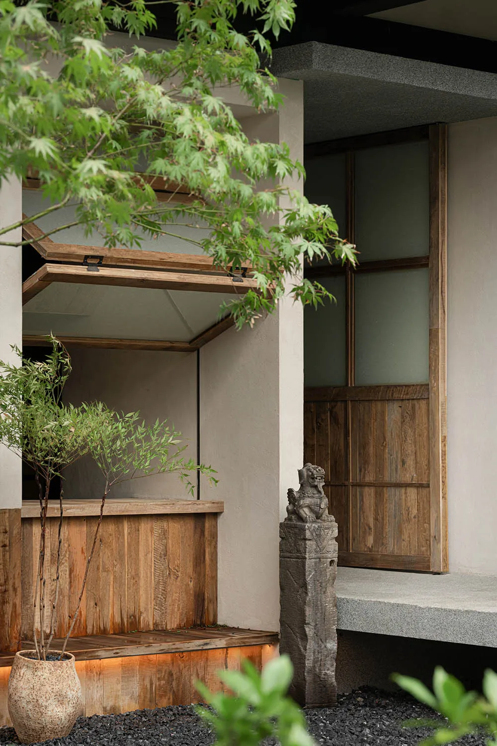Asian-style building with wooden doors and windows, surrounded by greenery and featuring a mix of wood and stone elements