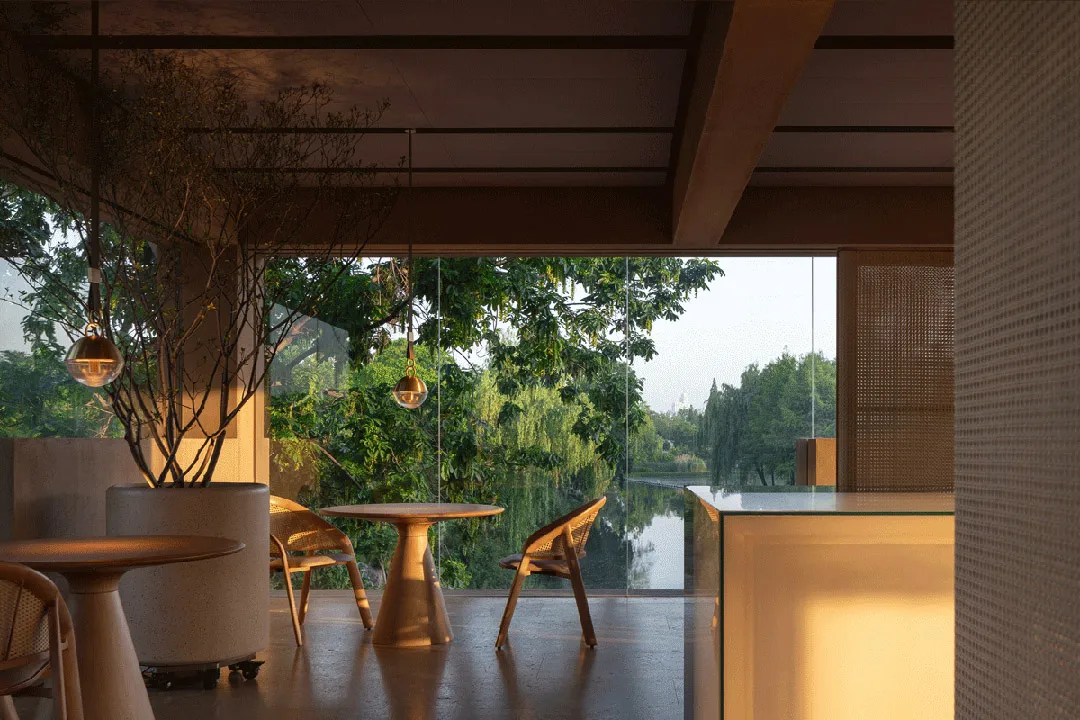 Open living area with a dining table, couch, chairs, and wooden walls, featuring large windows for natural light