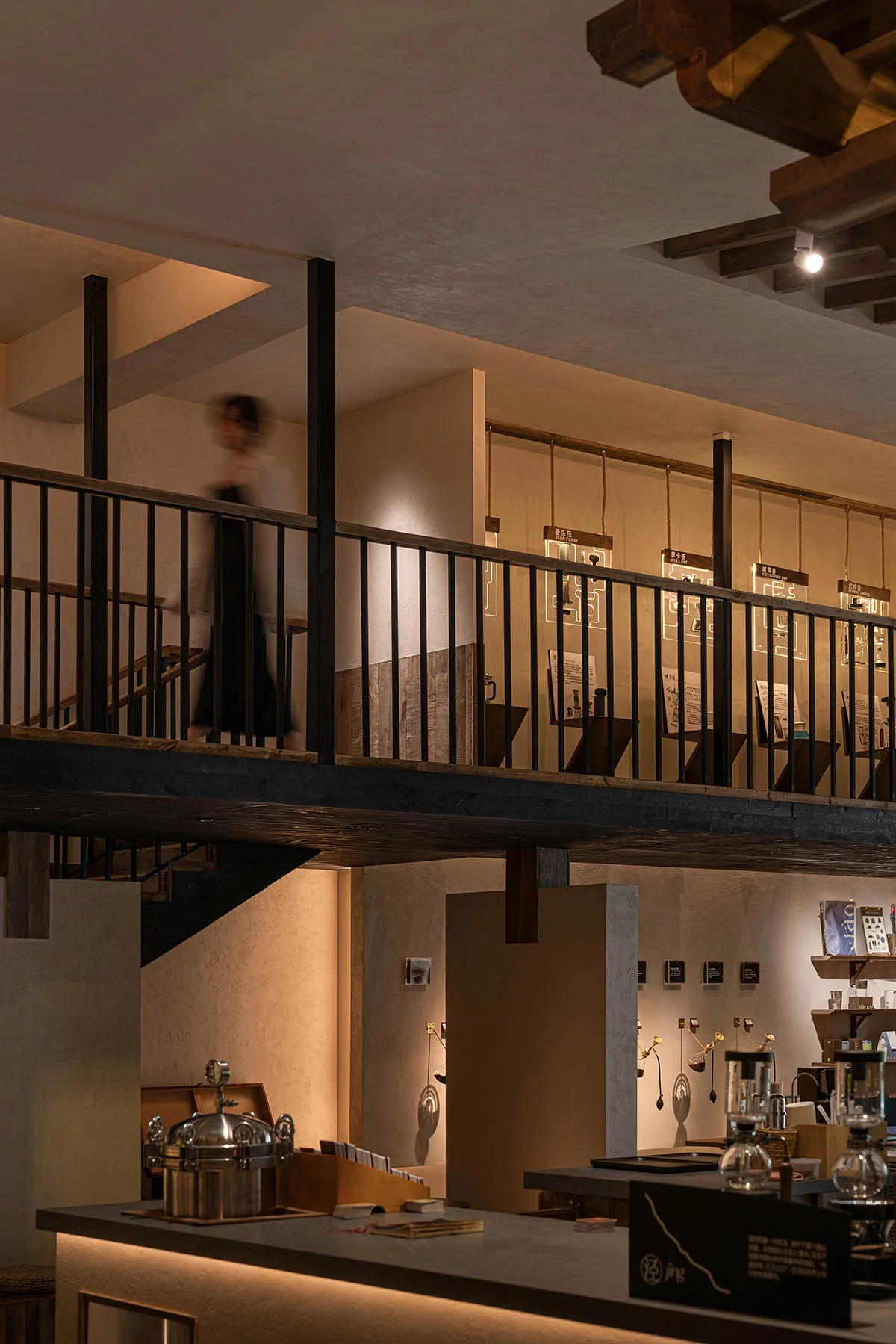 A calm and inviting interior space with a wooden staircase, stone elements, and soft diffused lighting, featuring visitors exploring the exhibits