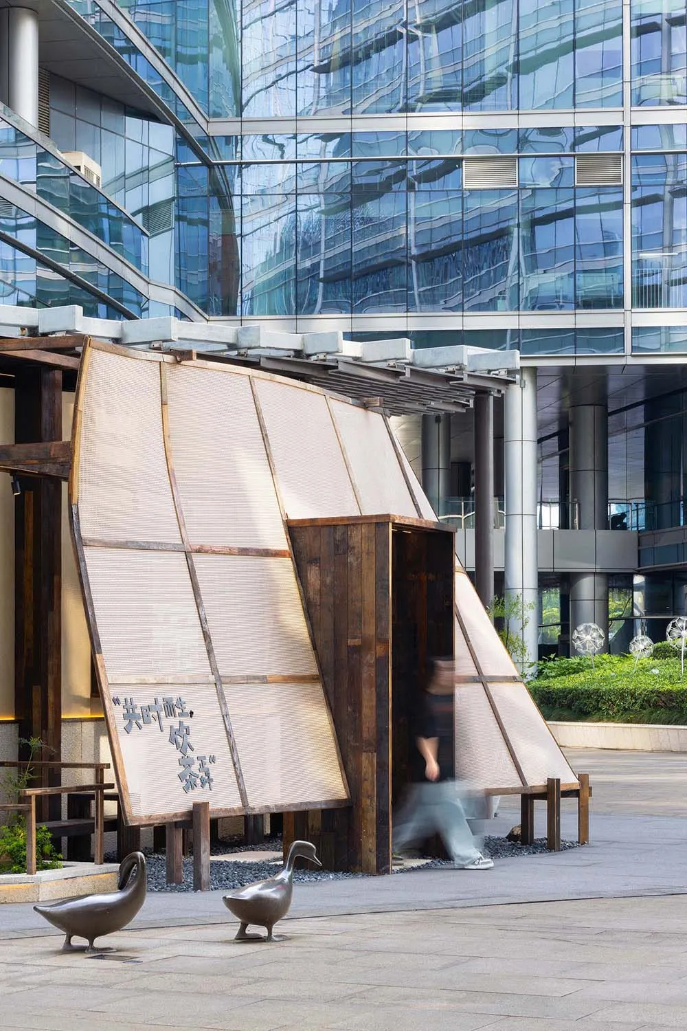 A woman walks past a modern building with glass windows and a contemporary design in a busy urban environment