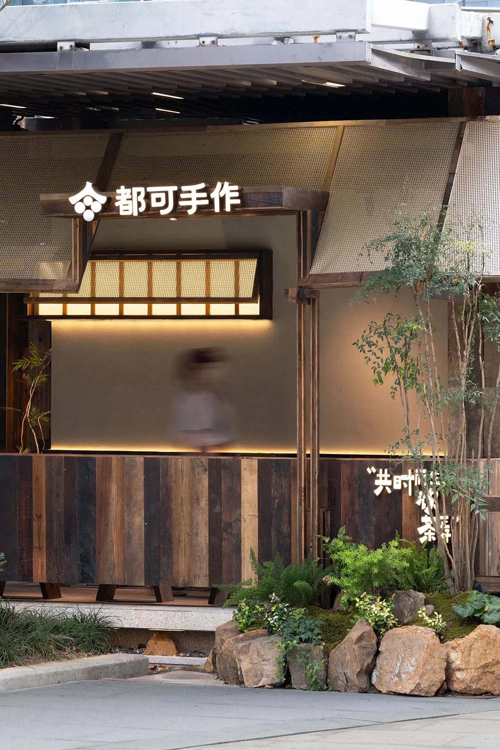 A woman walks through the entrance of an Asian restaurant with a warm and inviting atmosphere, surrounded by wooden elements and potted plants
