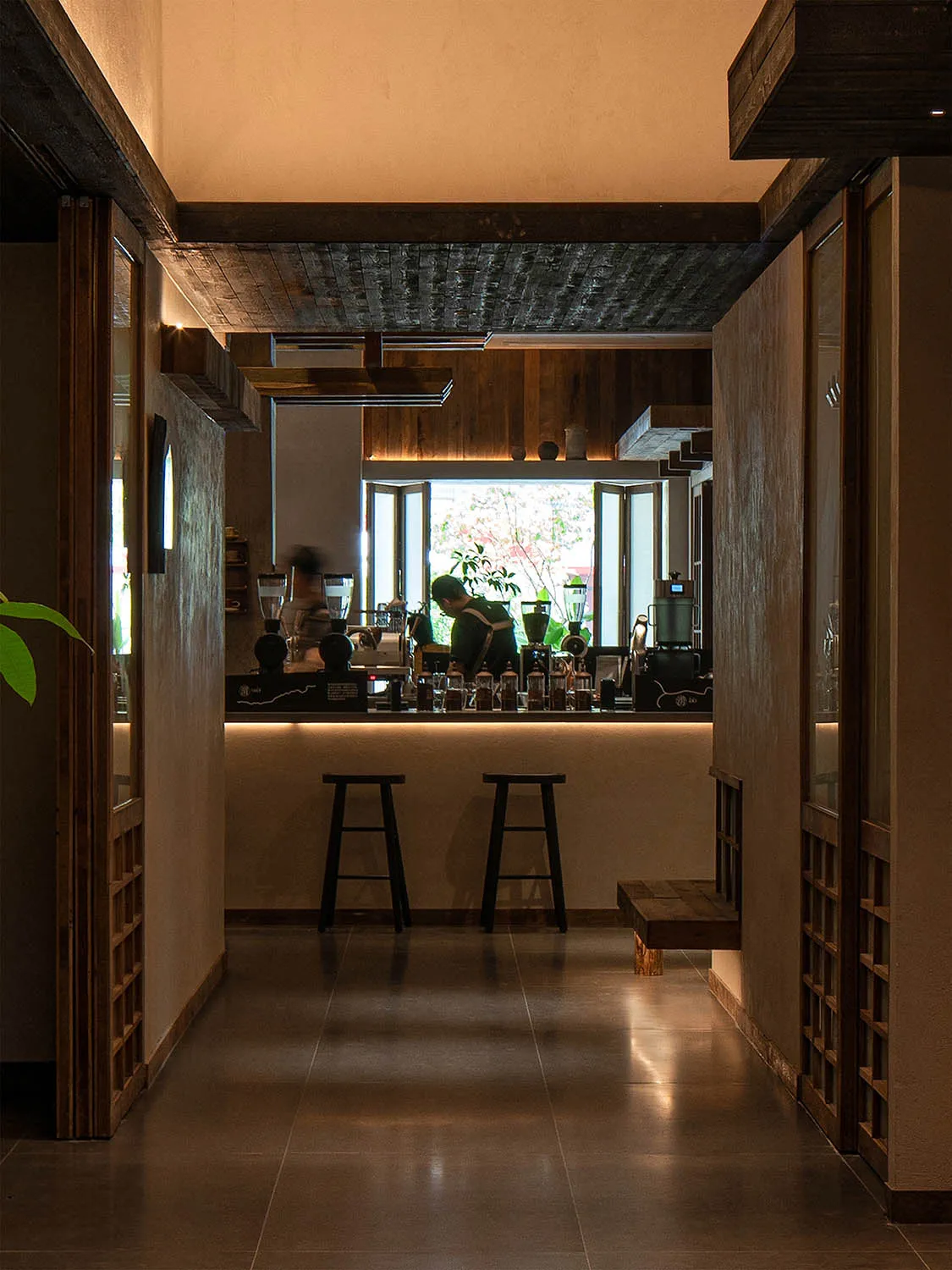 A cozy cafe interior with a wooden bar, potted plants, and various items on the counter, set for a welcoming atmosphere