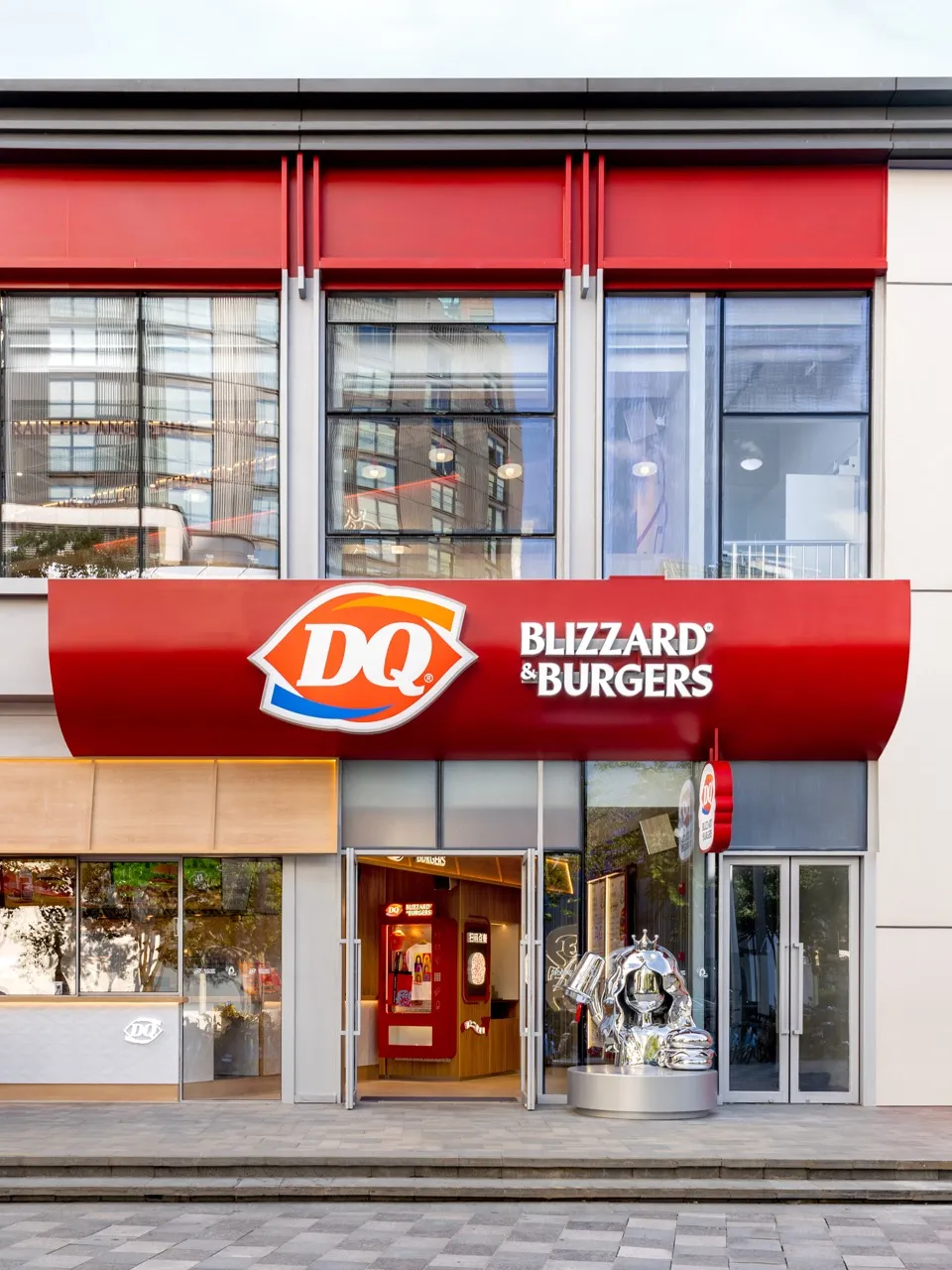 紅色屋頂現代餐廳的外觀，擁有眾多窗戶和大大的「DQ Blizzard Burgers」招牌，側邊有兩個時鐘
