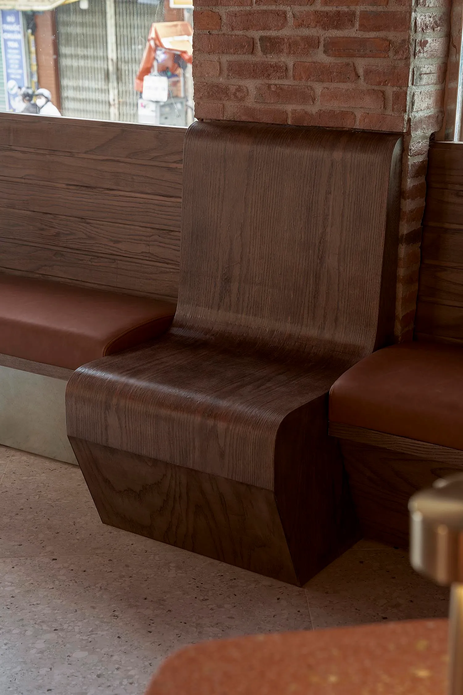 A room with a wooden bench and brick wall, featuring a brown leather seat and natural light from a window