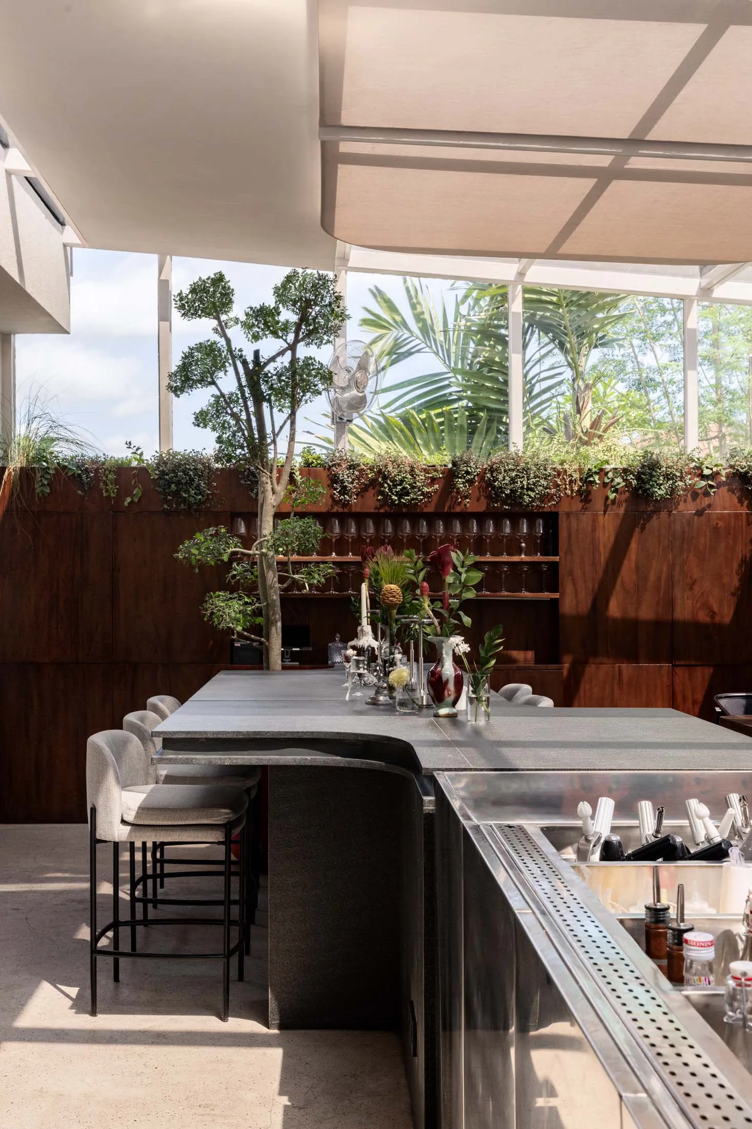 Modern restaurant interior with a large dining table, chairs, and potted plants, featuring clean lines and minimalistic design elements