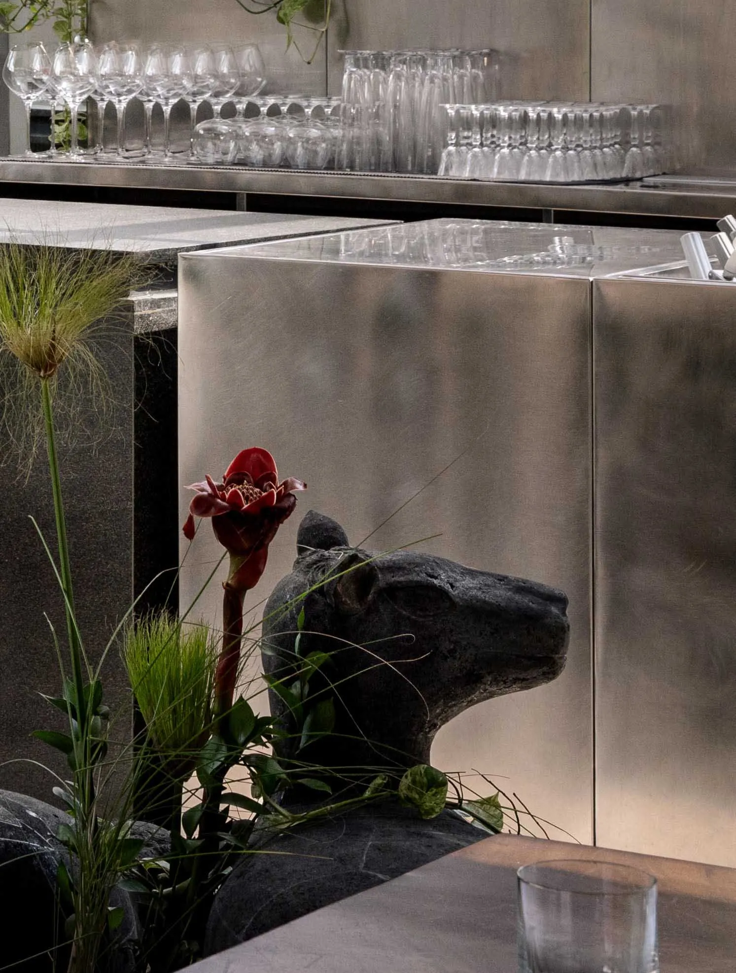 A modern interior design featuring a metal sculpture of a dog on a stone pedestal with a red flower and wine glasses, creating a sophisticated and inviting atmosphere