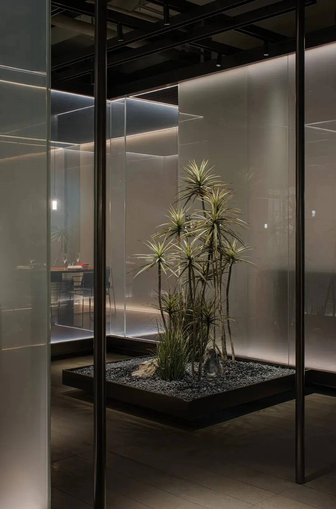 A dining room with a glass wall, natural light, potted plants, a dining table, and decorative vases