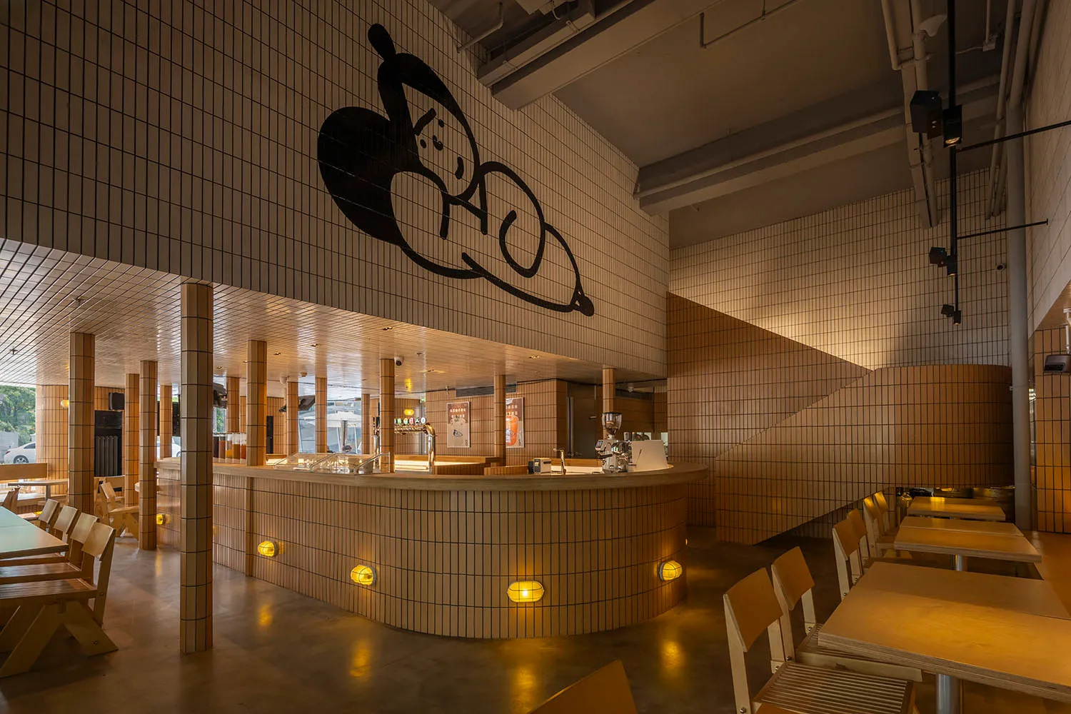 A restaurant interior with a counter and stairs, featuring a unique black and white mural on the walls, and comfortable seating areas with chairs