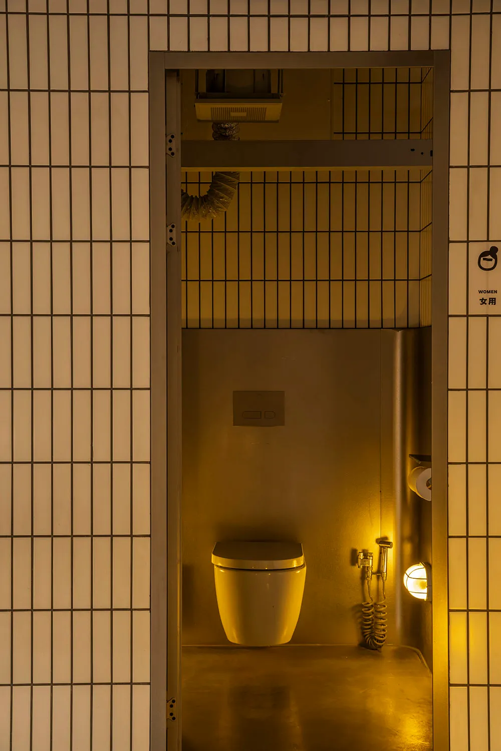 A functional bathroom with two metal sinks, a white toilet, and a mirror above one of the sinks, set against a yellowish background
