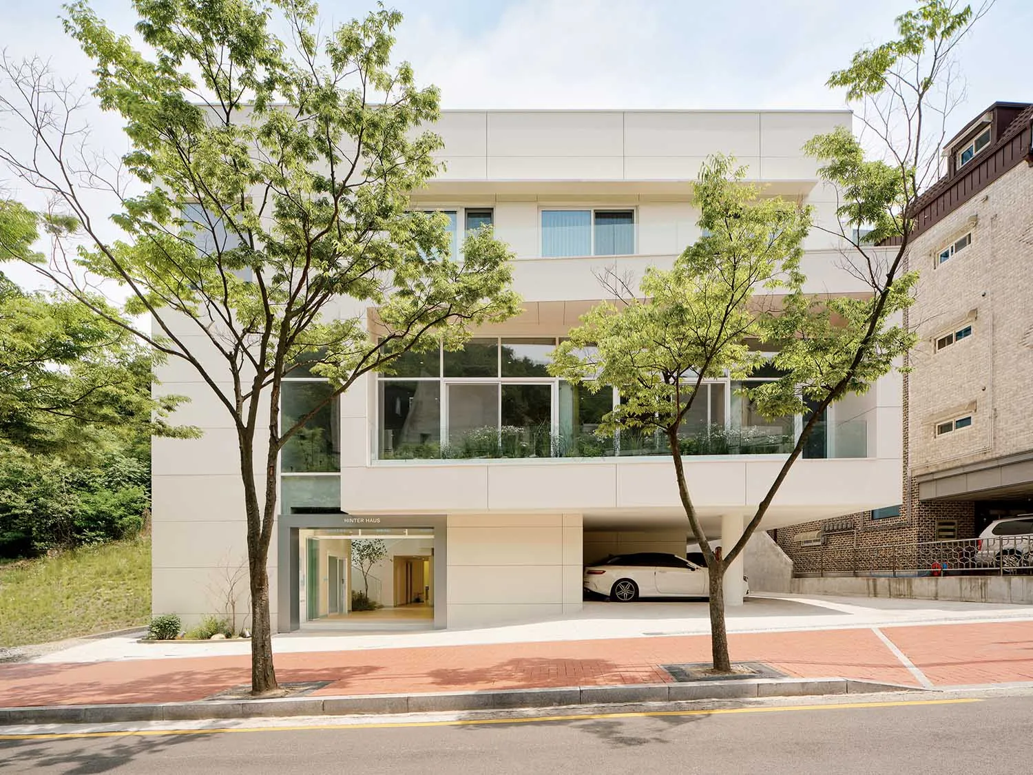 A modern building with a large glass window, surrounded by a parking area with two cars, under natural daylight