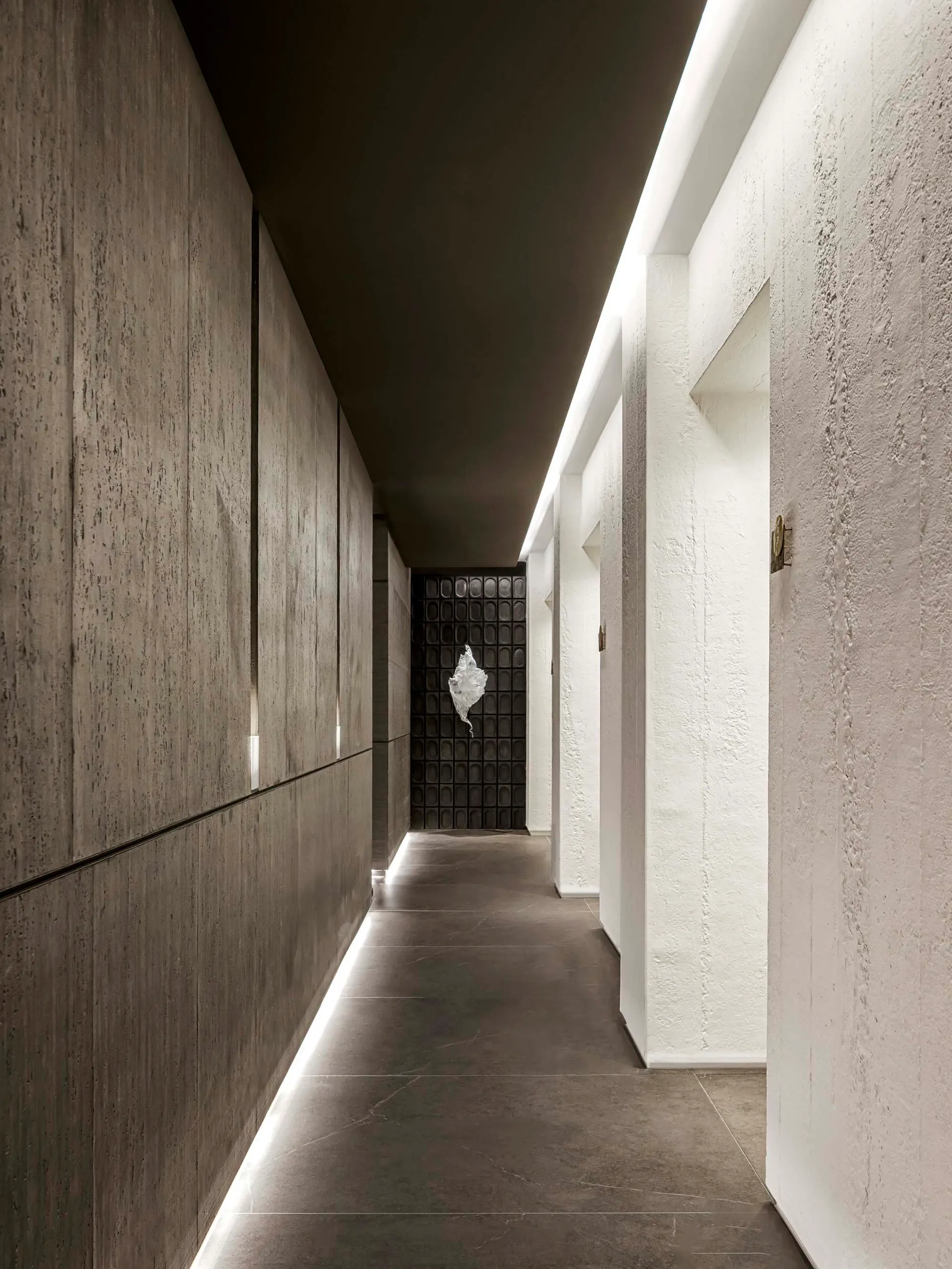 A dimly lit hallway in an old building with white walls and floors, featuring two doors on either side