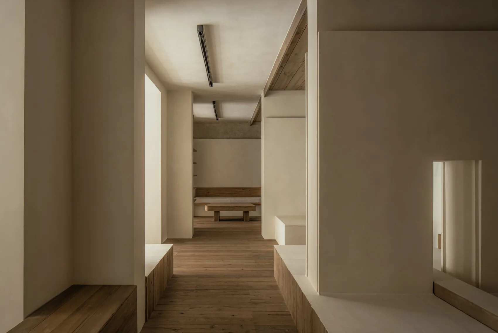 Empty white room with wooden floors and walls, featuring two benches and a calm atmosphere