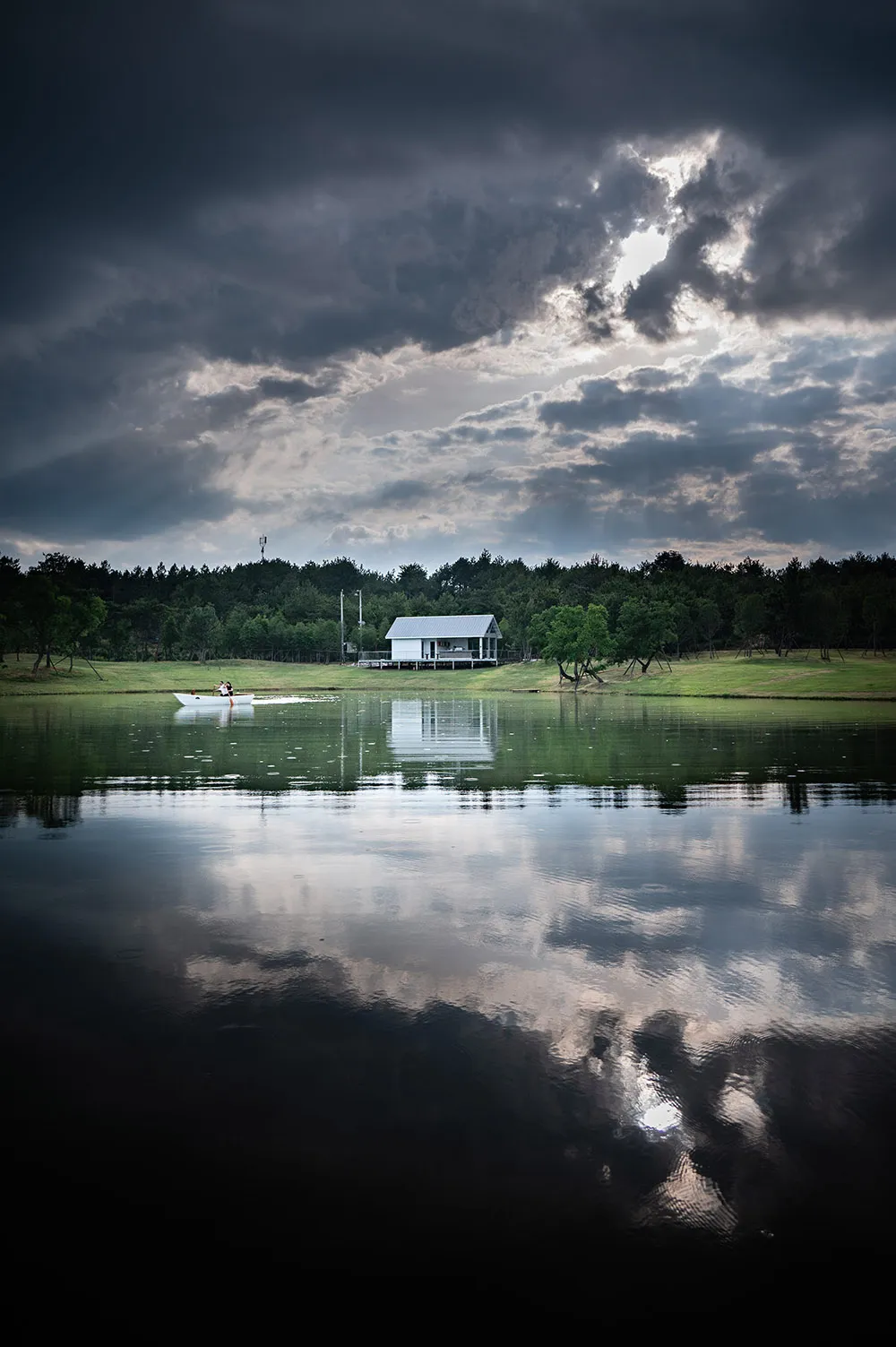 A serene lake surrounded by trees and houses, with a couple in a boat on the water