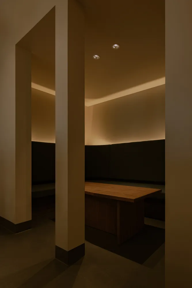 Dimly lit room with a wooden table and two benches, surrounded by white walls and a simple atmosphere