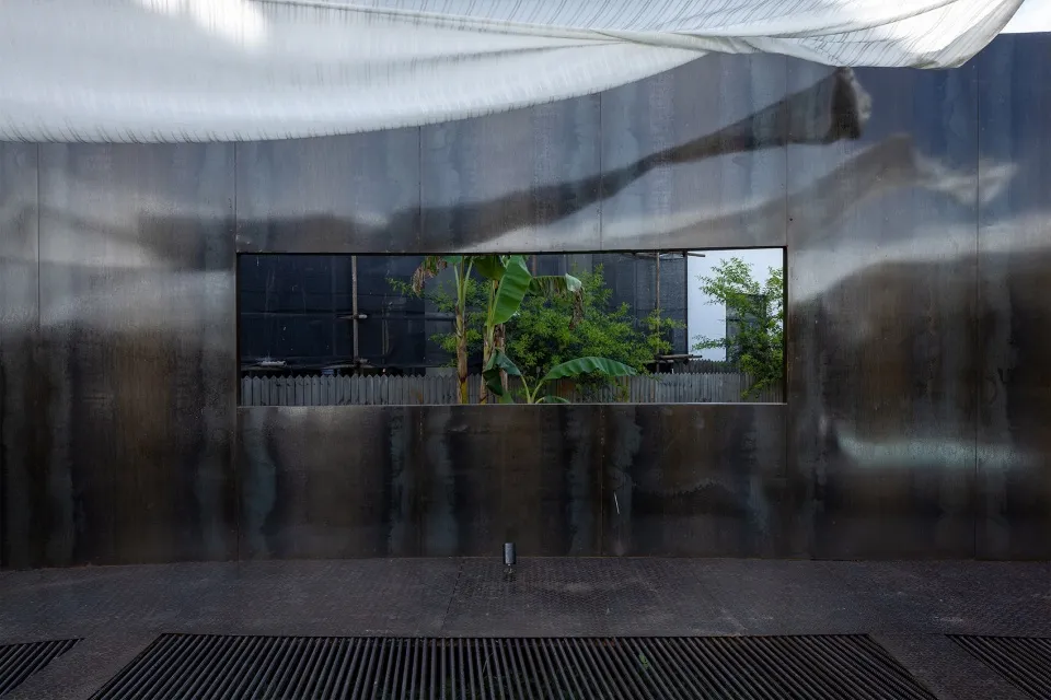 Industrial building with a metal wall and a window, surrounded by two banana trees