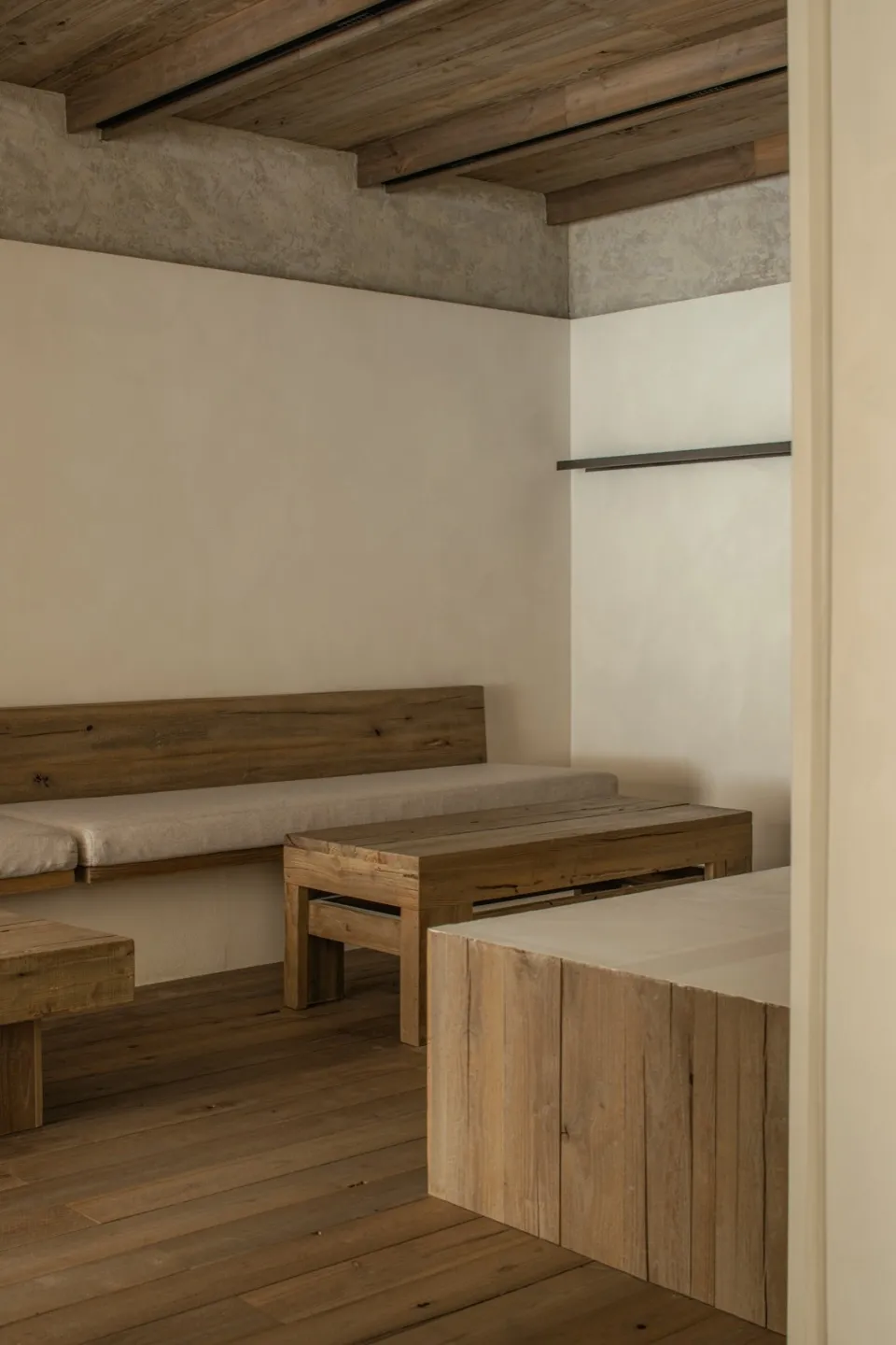Small room with wooden floors, white walls, two beds with benches, and a dining table, creating a cozy and functional space