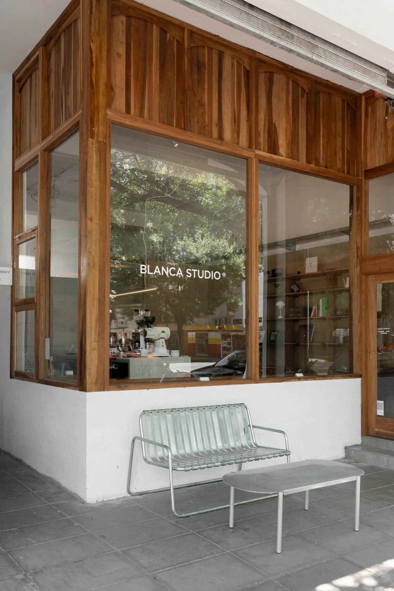 Modern building exterior with a metal bench in front of a large glass window, a car parked nearby, and an urban atmosphere