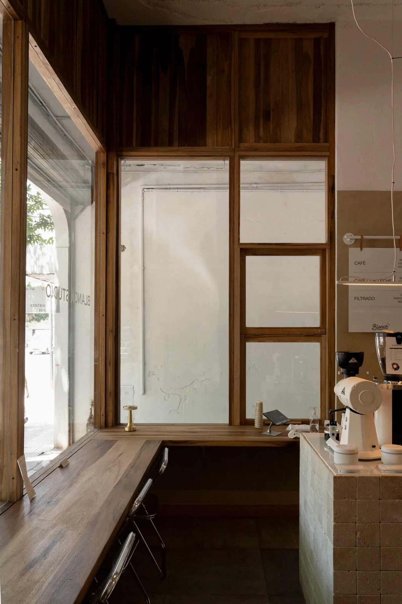 A warm and inviting coffee shop interior with a counter, cappuccino machine, sink, chairs, and a dining table in the background
