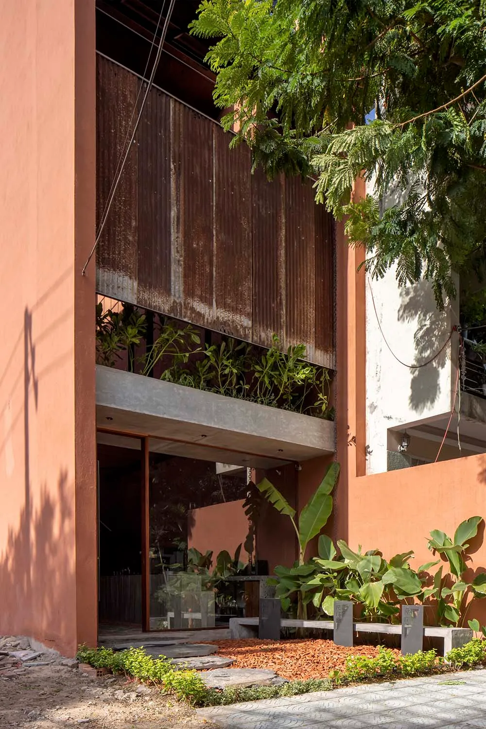 Modern house with a red brick exterior, large window, and doorway, surrounded by potted plants