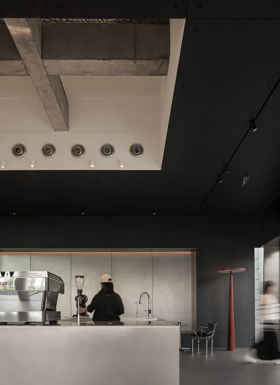 A modern restaurant interior with a counter featuring a metallic finish, black and white walls, and two people in the scene