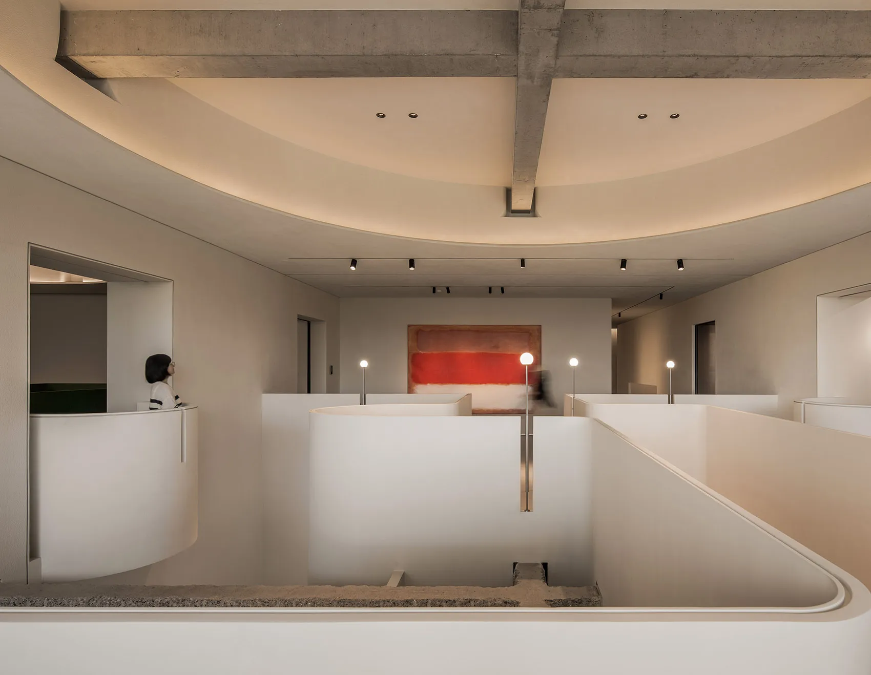 A white interior space with a spiral staircase surrounded by artwork and people admiring the displayed pieces