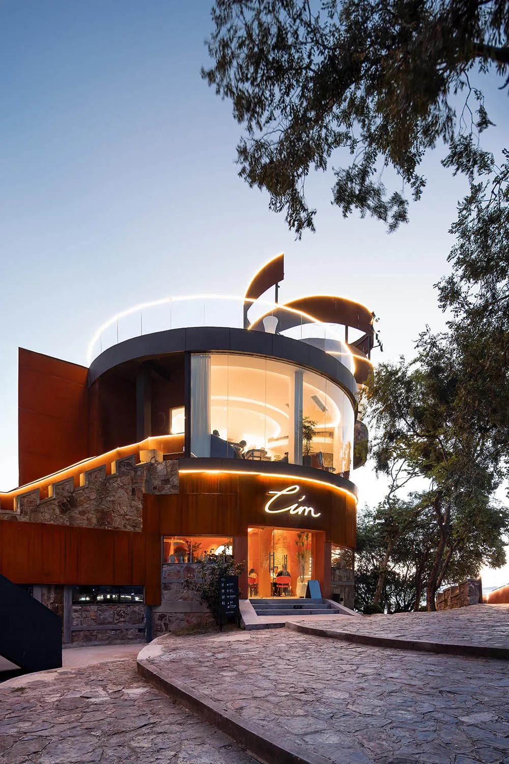 A modern building with a glass dome and red brick exterior, featuring a spacious lobby with natural light, potted plants, and seating areas