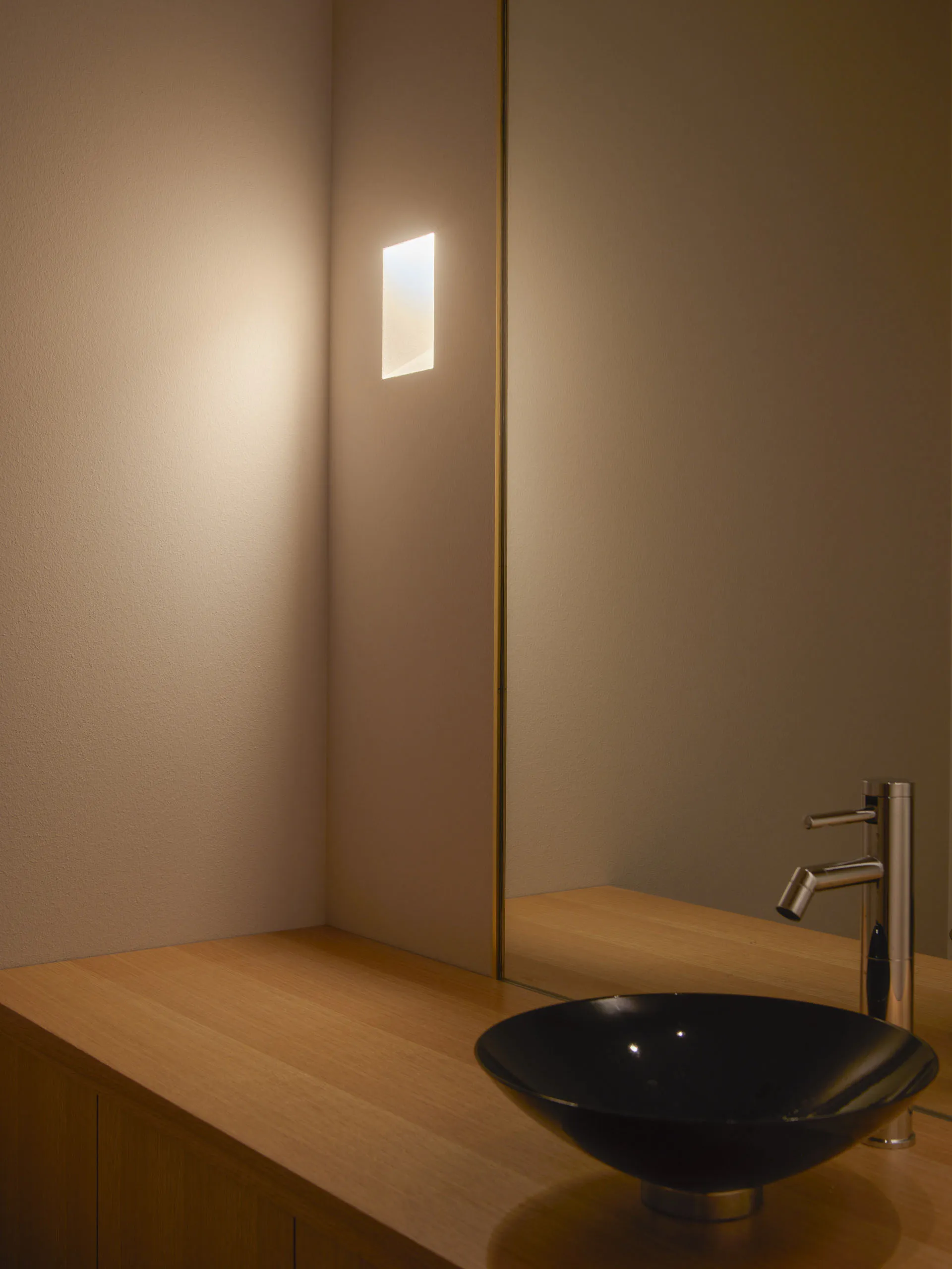 A clean bathroom with a sink on the right, a mirror above it, and two lights, one near the left edge and one near the center, creating a well-lit and inviting atmosphere