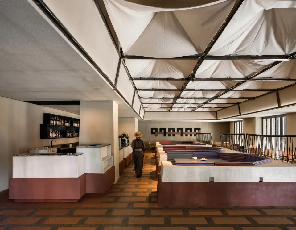 A casual restaurant with a dining table, chairs, and bottles, featuring a person walking through the space, with a focus on socializing and enjoying food and drinks in a comfortable environment