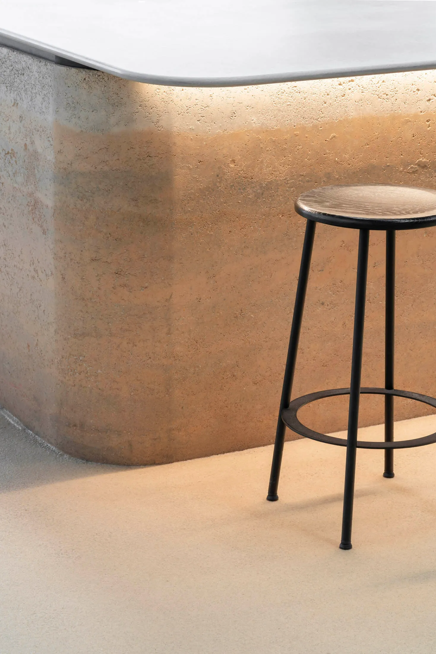 A minimalist space with a metal stool on a concrete floor, suggesting an industrial design style