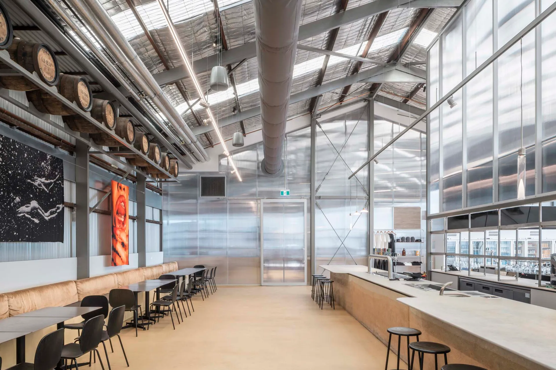 Industrial open space with a dining table and chairs, surrounded by a bar, with natural light coming in through windows or skylights