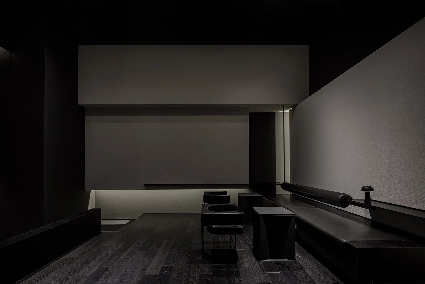 Empty dark room with a black wall and wooden floors, featuring several chairs placed throughout the space