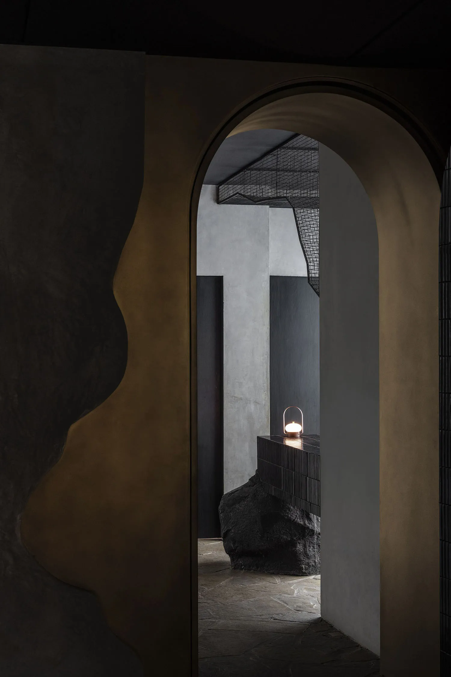 Modern entrance with concrete walls, black pillars, and a gold-framed doorway, illuminated by a nearby light source