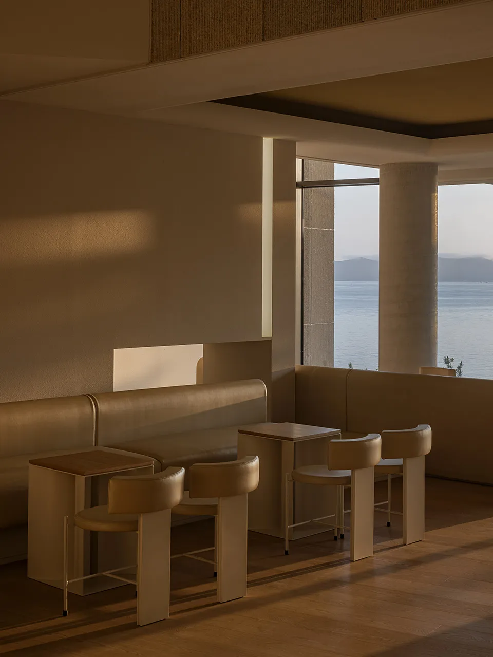 A warm and inviting cafe with a large window overlooking the ocean, featuring comfortable seating and natural light