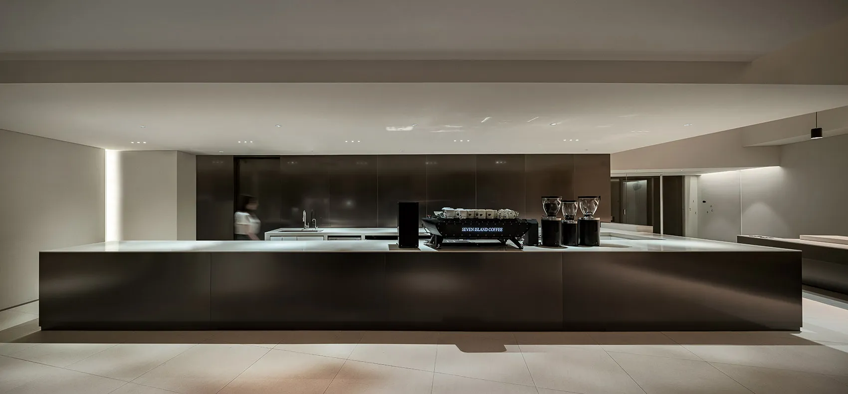 Modern kitchen with black countertops and cabinets, featuring two sinks, a coffee maker, and an oven, with cups scattered around the space