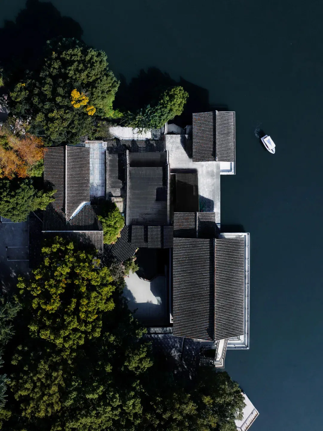 Asian-style house near a body of water with a black roof, surrounded by trees and a boat docked nearby