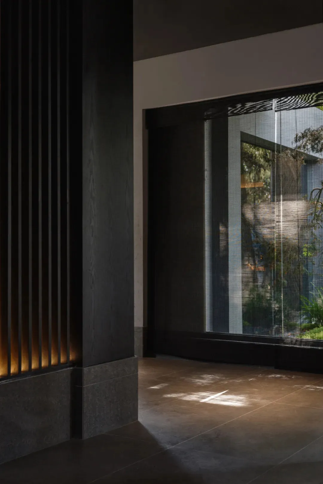 Dimly lit interior space with a black doorway, window with blinds, and potted plants on either side