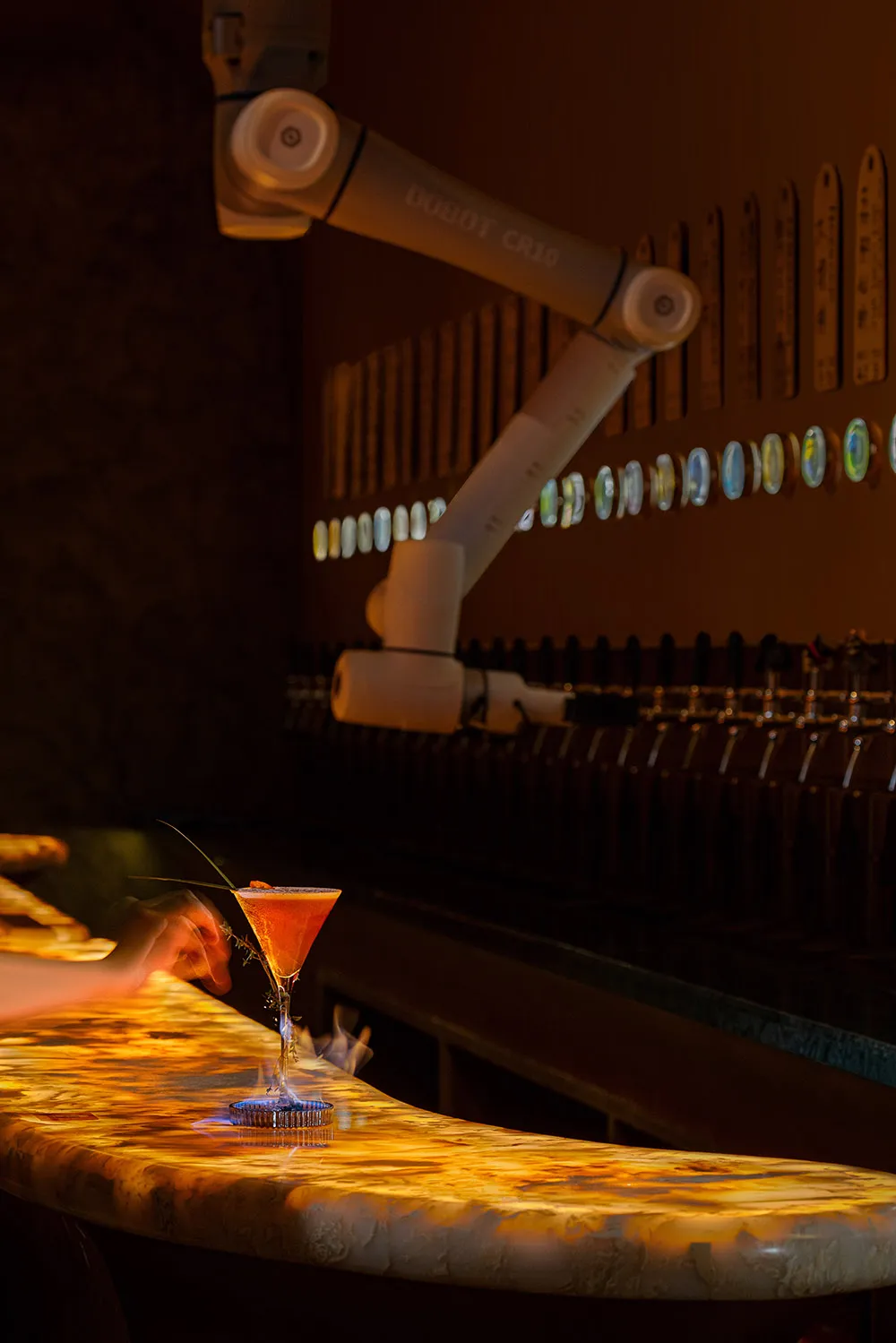 A woman sits at a bar with a martini, surrounded by bottles and a relaxed atmosphere