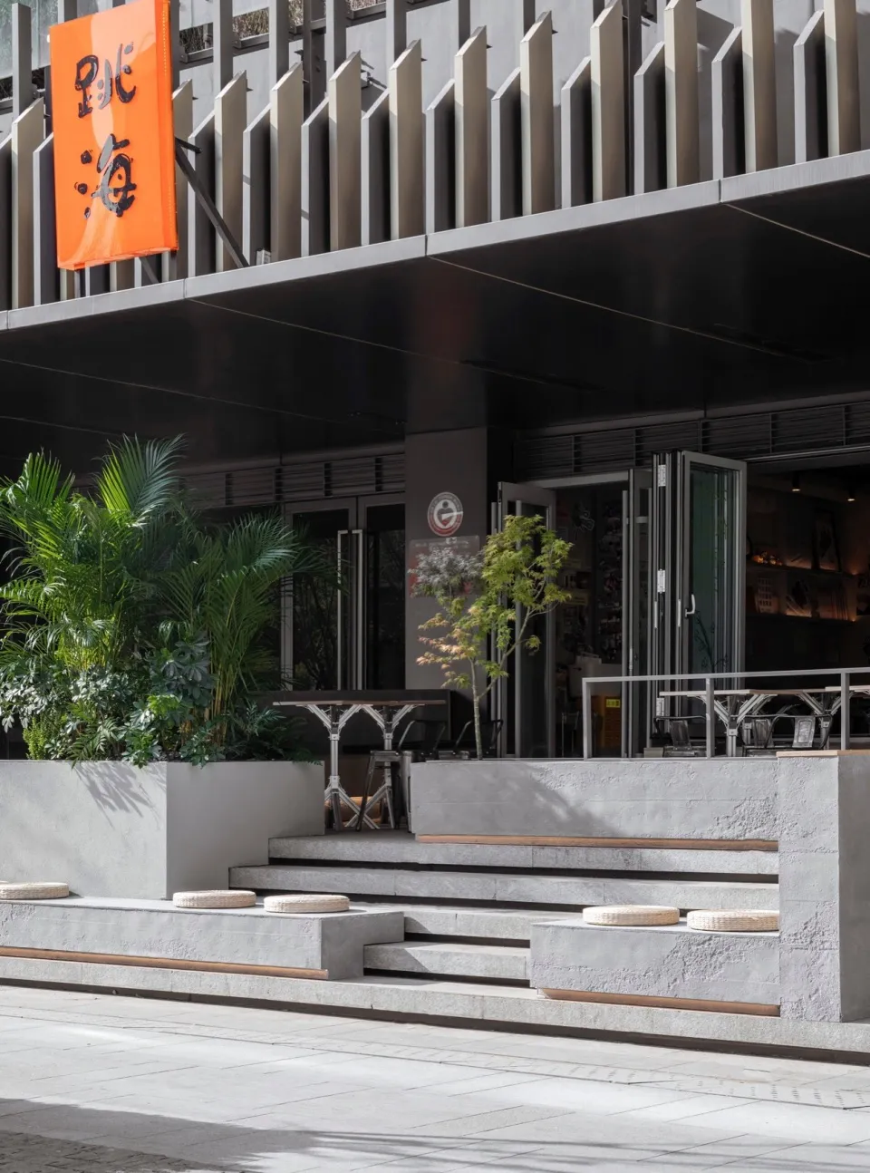 A calm exterior building facade with a staircase, two benches, and a potted plant, inviting a sense of relaxation