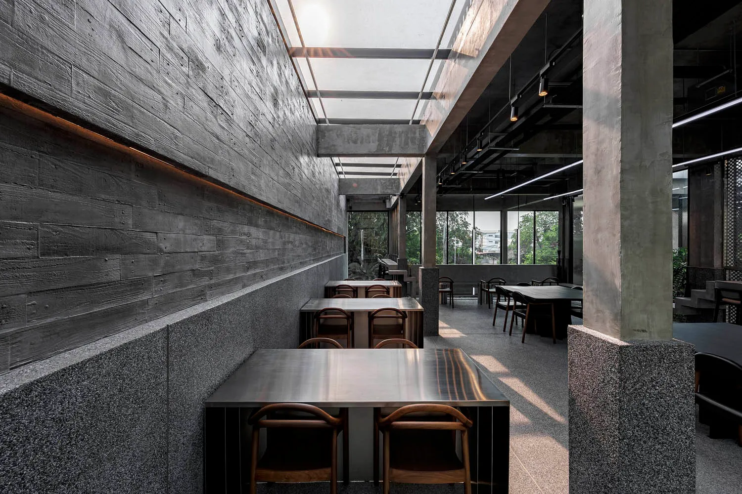 A modern restaurant interior with grey stone walls, numerous dining tables, and comfortable seating