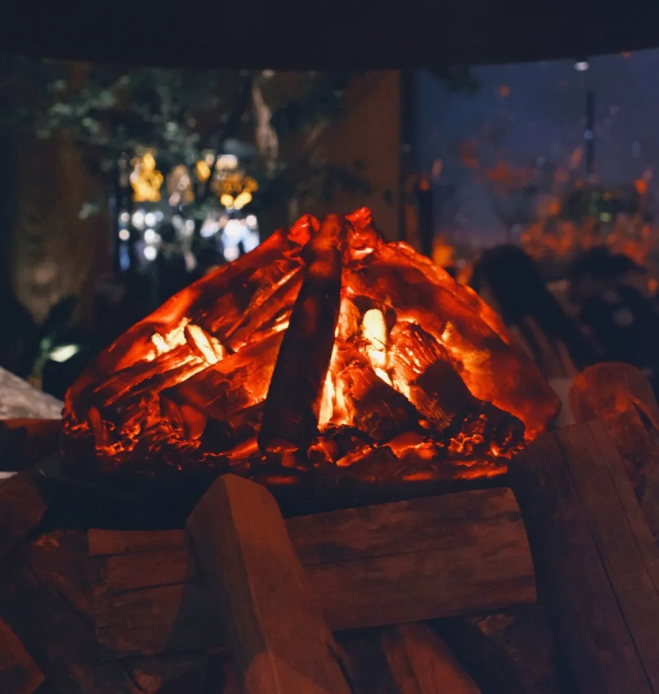 A warm and inviting living room scene with a lit fireplace, wooden design, and people gathered around