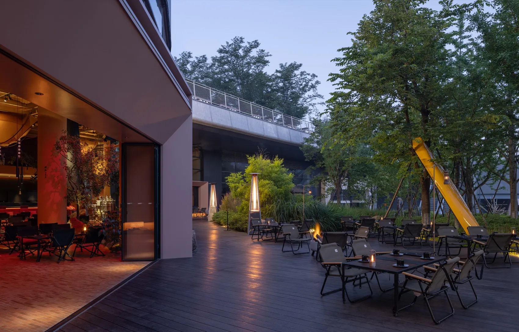 A restaurant patio at night with tables, chairs, umbrellas, candles, and a bridge, featuring wood flooring and a warm atmosphere