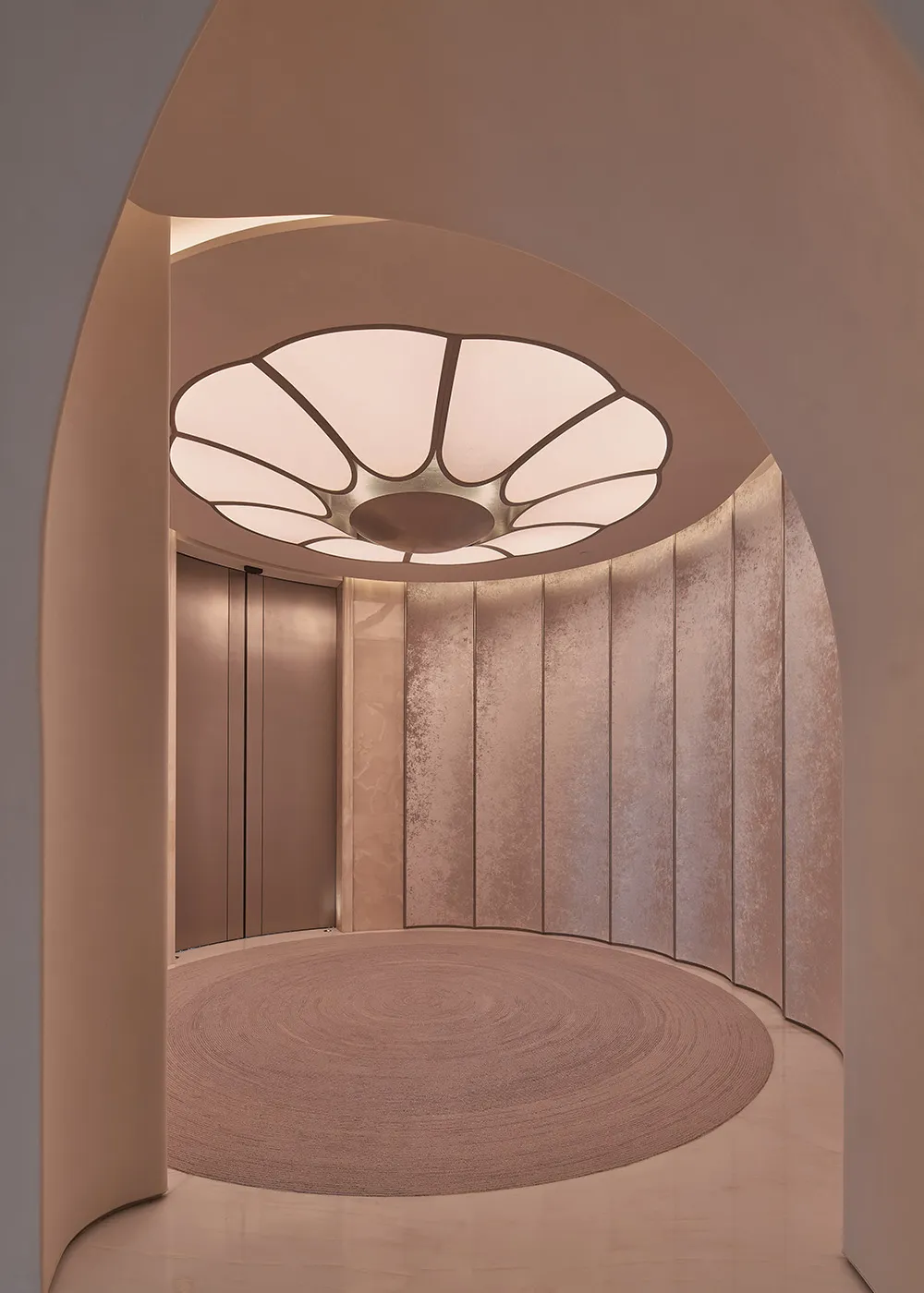 A warm hallway with pink and white walls, a wooden circular design element, and a doorway leading to another part of the building