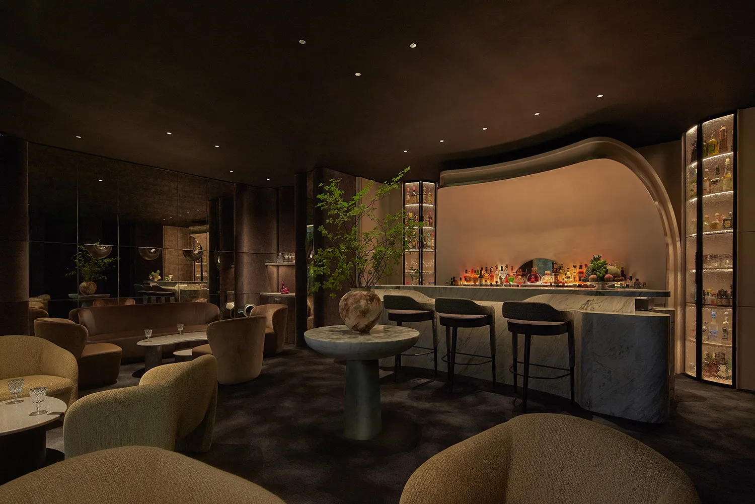 A sophisticated bar area with a large wooden counter, multiple chairs, and a smaller bar on the right, creating a comfortable atmosphere for patrons to enjoy their drinks and socialize