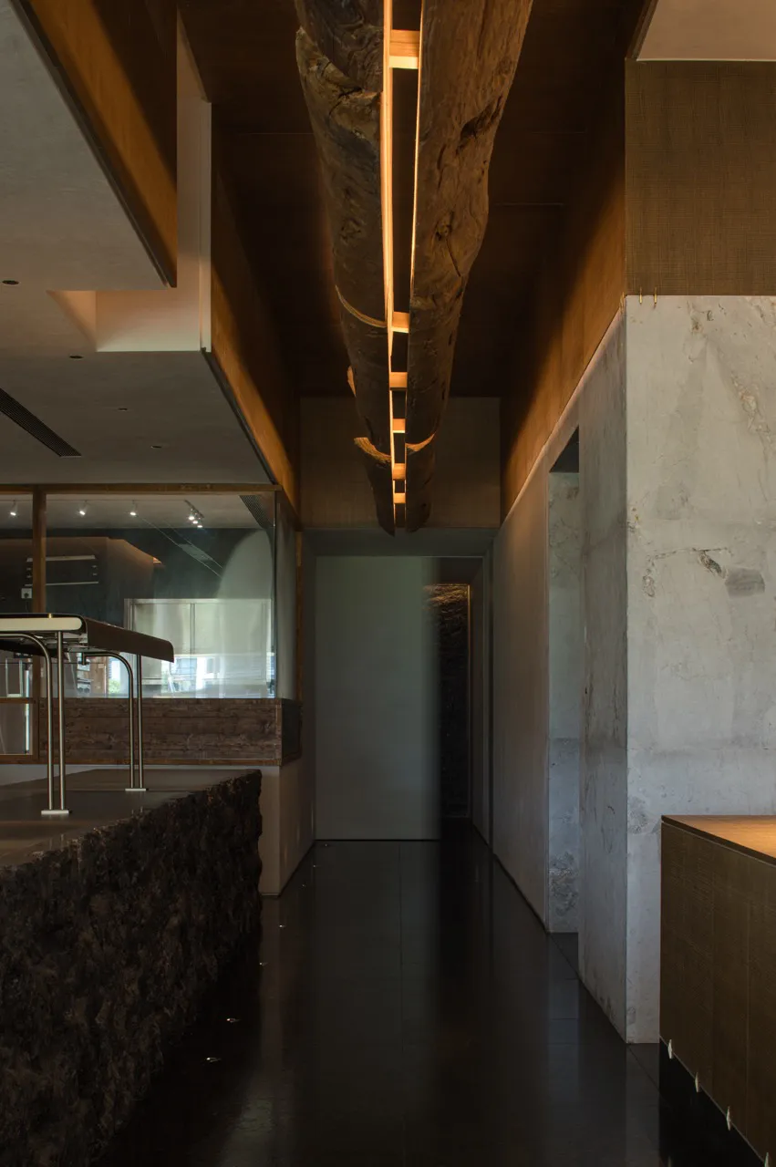 Modern kitchen with a stone finish, a dining table, chairs, and a refrigerator, set in a dimly lit space