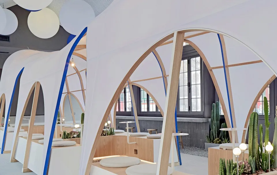 A modern cafe with a white canopy structure, wooden elements, and potted plants, creating a comfortable and inviting atmosphere for socializing and dining