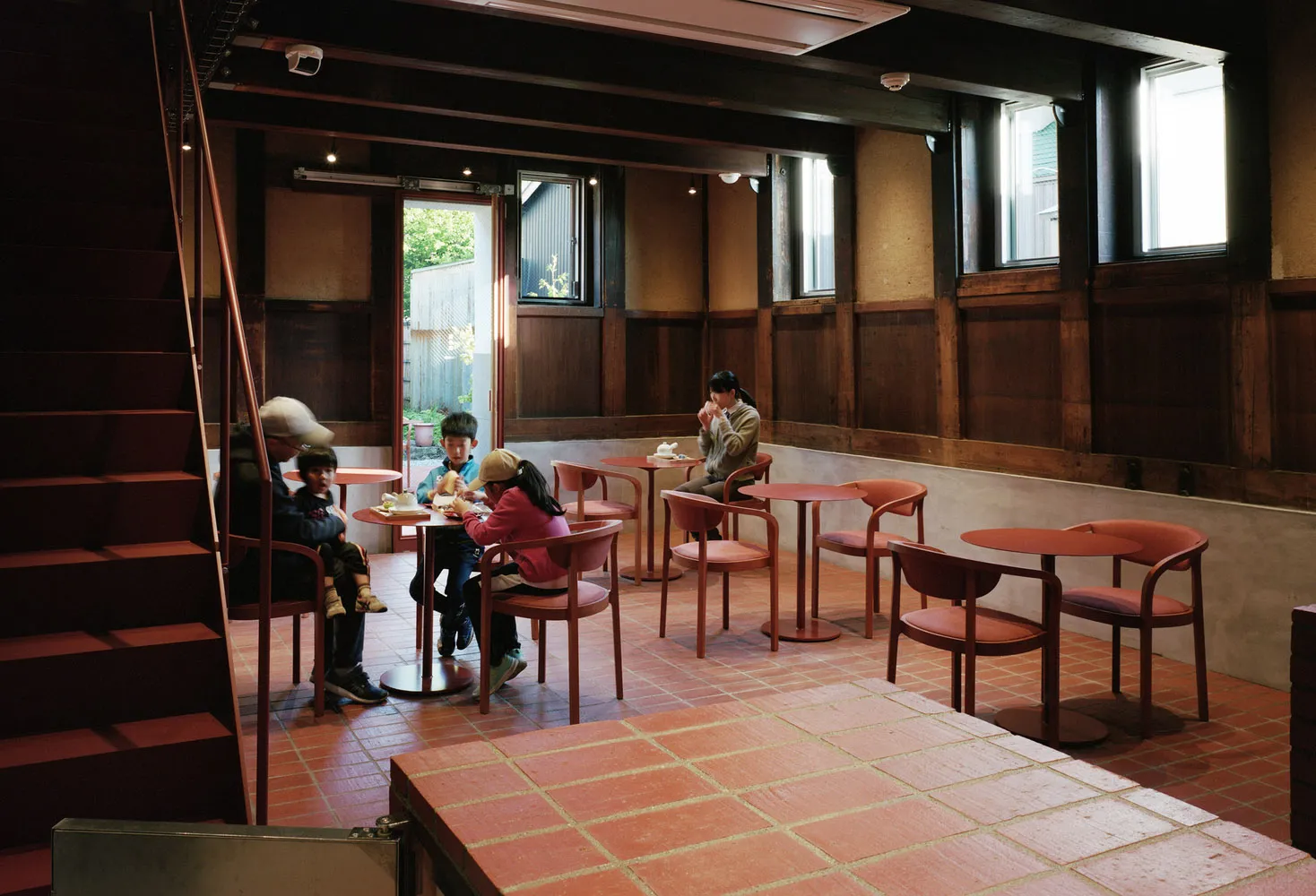 A casual dining area with multiple tables and seating options, including benches and chairs, with people gathered together