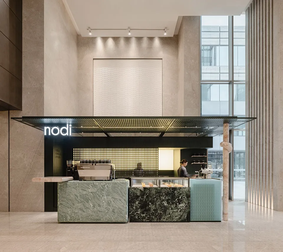 A modern cafe with a counter, couches, and a dining table, featuring marble and wood elements, natural light, and a warm atmosphere