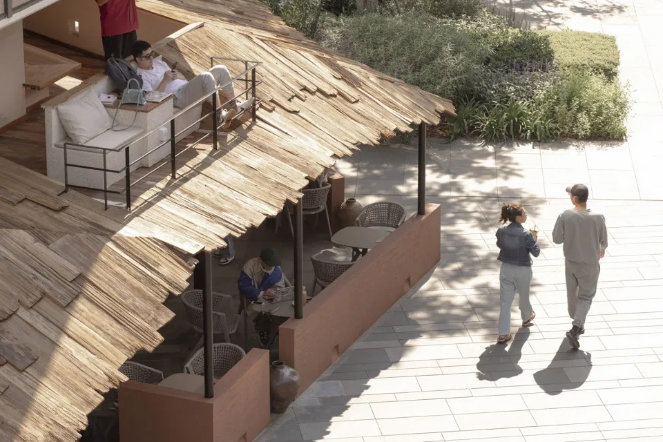 Outdoor restaurant with a thatched roof, tables, and chairs, surrounded by people dining and socializing