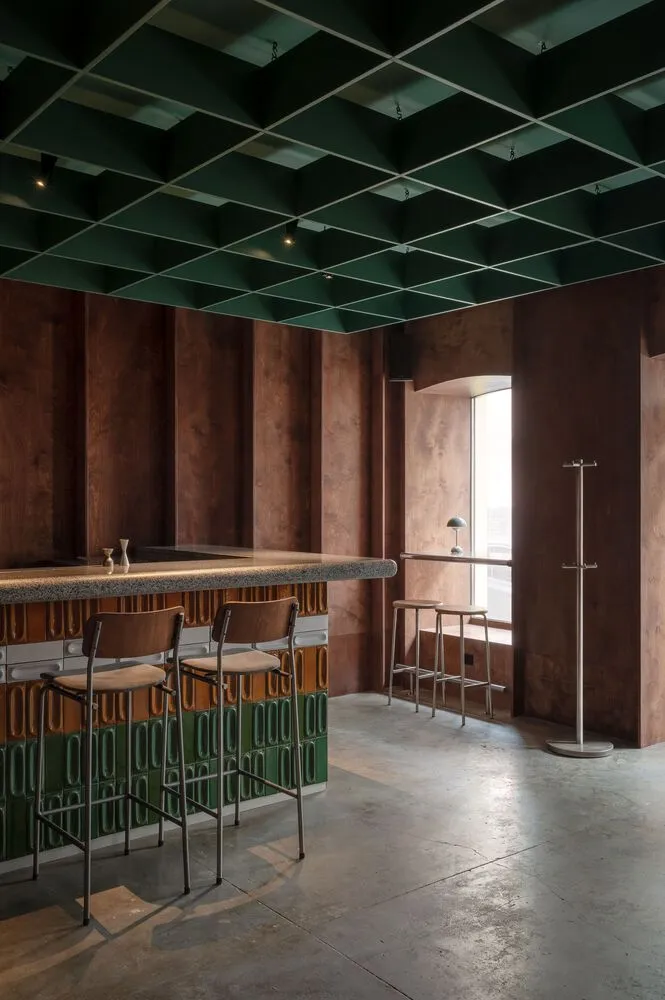A modern bar area with a green-hued atmosphere, featuring a counter with stools, a dining table, and three chairs, set in a comfortable and inviting space
