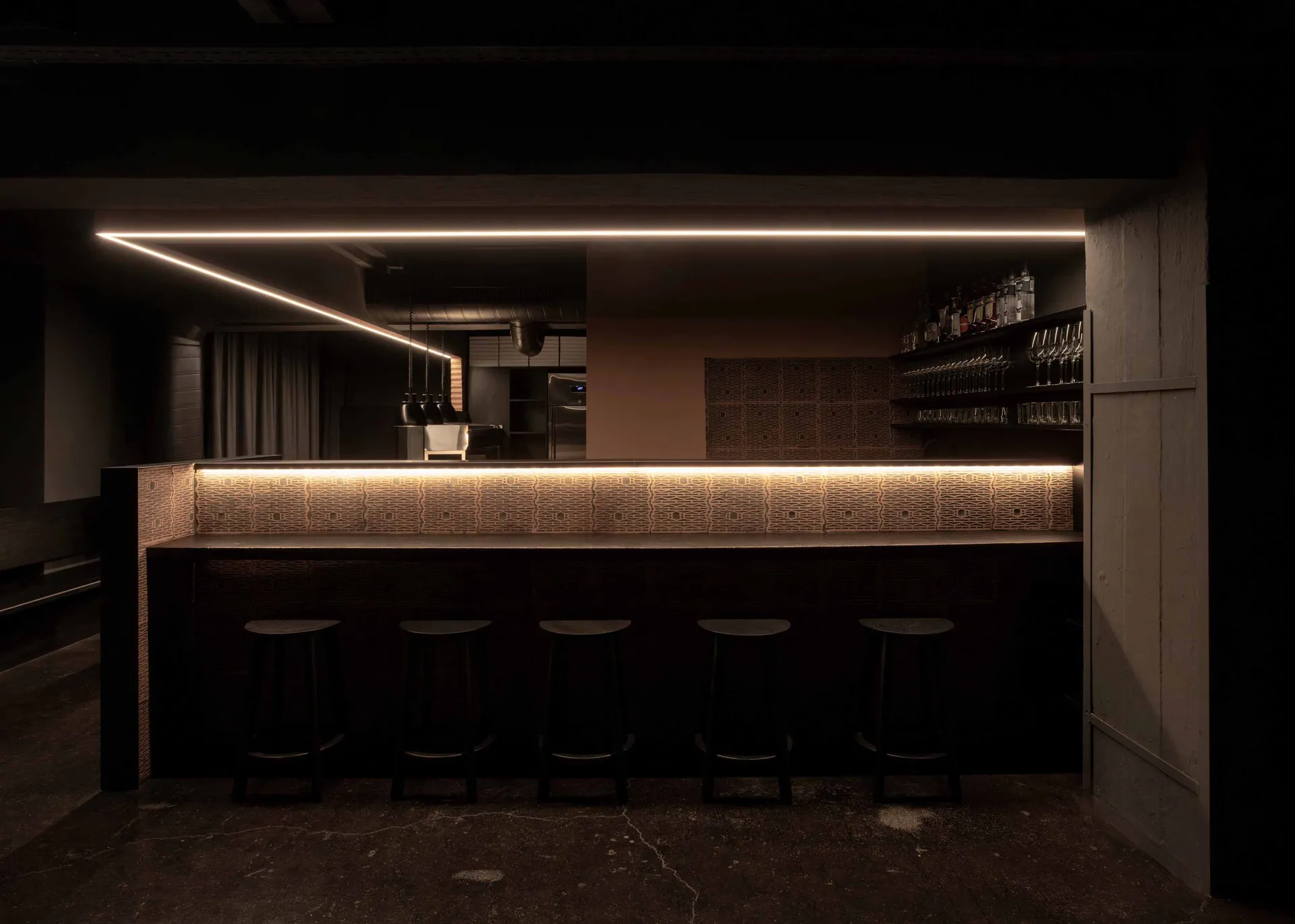 A modern bar area with a black countertop, brown wall, and four stools, creating an inviting and comfortable atmosphere